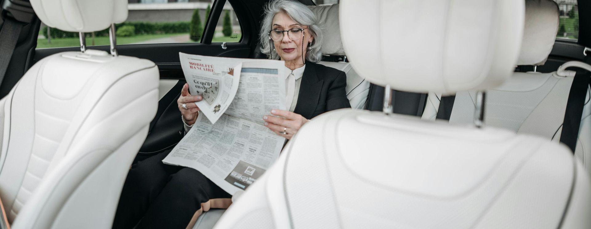 Elderly woman in car reading a newspaper, showcasing a moment of relaxation and focus.