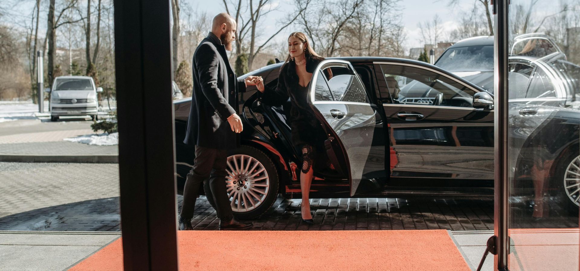 A couple stepping out of a luxury car onto a red carpet in an upscale outdoor setting.